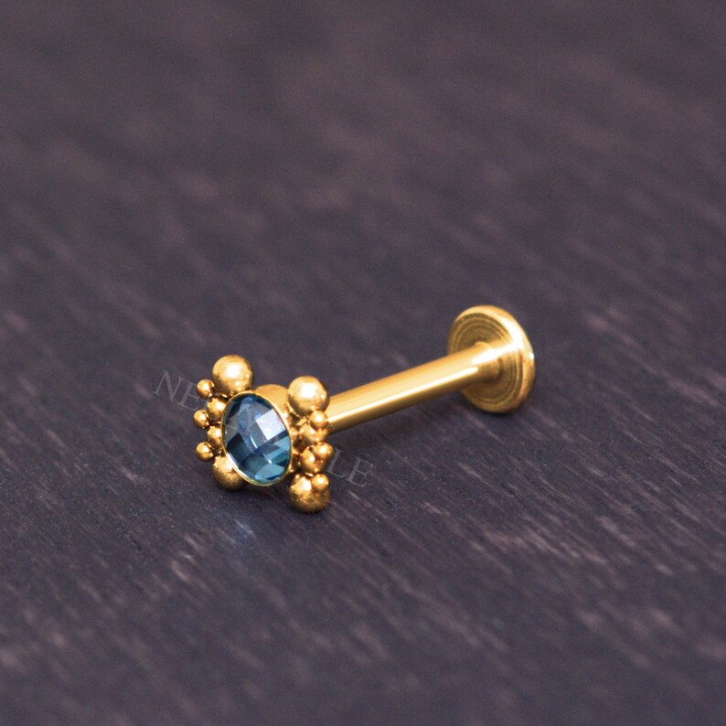 May include: Gold body jewelry with a blue gemstone and a beaded design.