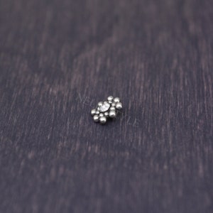 May include: A silver flower-shaped body jewelry with a clear crystal in the center.