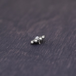 May include: A silver body jewelry piece with a clear gem in the center and five silver balls surrounding it. The jewelry piece has a screw-on back.