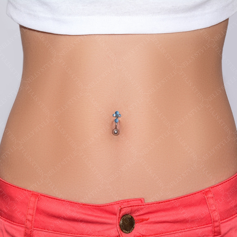 May include: A belly button ring with a silver-colored barbell and a cluster of small, light blue gemstones at the top. The bottom features a small, silver-colored ball. The skin around the navel is visible.