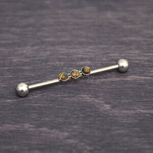 Puede incluir: Una barra de plata con cuatro piedras de &oacute;palo iridiscentes. La barra es una joya de piercing corporal.