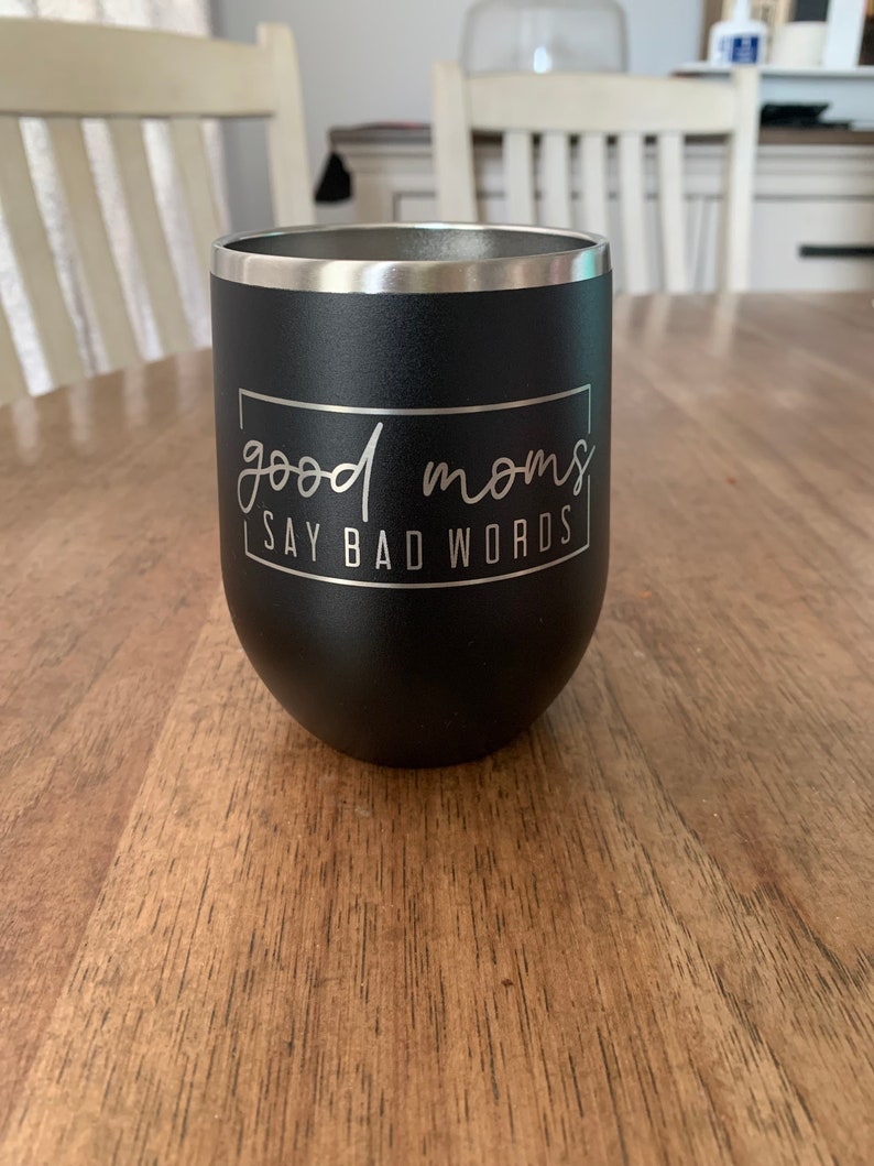 Może przedstawiać: Czarny kubek ze stali nierdzewnej z białym napisem "good moms say bad words" w odręcznym stylu.