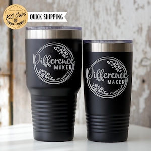 May include: Two black stainless steel tumblers with a silver lid. Both tumblers have the words "Difference Maker" engraved on them with a floral design around the words. The smaller tumbler is on the right and the larger tumbler is on the left. The text "#Teacher Life" is engraved below the words "Difference Maker" on both tumblers.