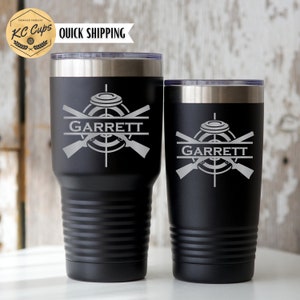May include: Two black stainless steel tumblers with a silver lid. The tumblers are engraved with a clay pigeon target, crossed shotguns, and the name "GARRETT".