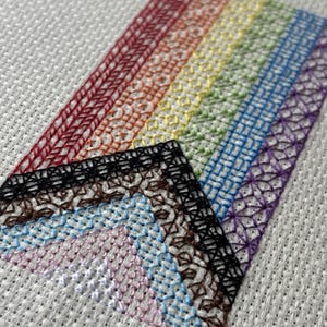 May include: Close-up of a cross-stitch sampler with a rainbow of colors. The sampler features various stitch patterns in red, orange, yellow, green, blue, and purple. Additional sections show black, brown, light blue, pink, and white stitching.