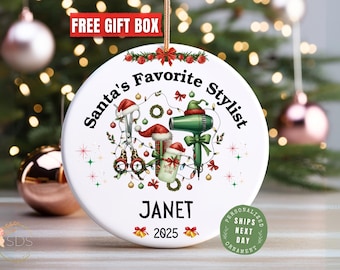May include: White ceramic Christmas ornament with the text "Santa's Favorite Stylist" and the name "Janet" below. The ornament features illustrations of salon tools and Santa hats. The year 2025 is also displayed.