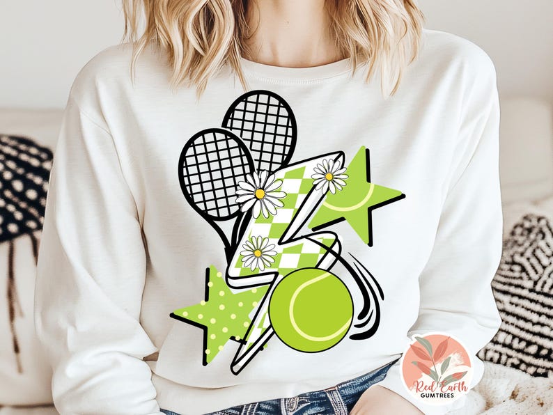 May include: White sweatshirt with a graphic design of two tennis rackets, a lightning bolt, a star, and a tennis ball. The design is in green, black, and white.