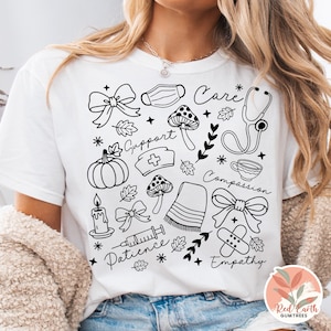 May include: White t-shirt with a black line art design featuring medical and autumn-themed illustrations. Includes a stethoscope, pumpkin, mushrooms, bows, and the words "Care", "Support", "Compassion", "Patience", and "Empathy".