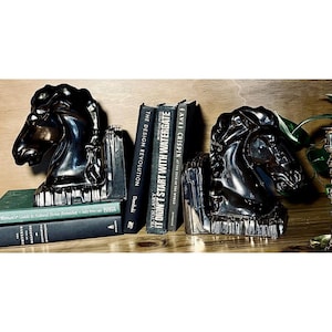 May include: A white ceramic mug with a black handle and the text "But First, Coffee" in a bold, black font. The mug is set against a blurred background, suggesting a cozy setting.