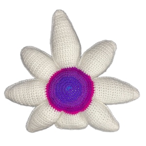 Può includere: Un grande fiore all'uncinetto fatto a mano con petali bianchi e un centro vibrante. Il centro passa da un viola intenso a un rosa brillante, con un tocco di blu al centro. Il fiore è un oggetto decorativo morbido e strutturato.