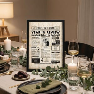 May include: A framed newspaper print titled "The 1966 Post Year in Review." The print features a wedding photo and text, set on a table with candles, plates, and glasses. The scene is lit by a lamp.