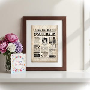 Pu&ograve; includere: Una stampa incorniciata di una pagina di giornale intitolata "The 1976 Post Year in Review". La stampa &egrave; in una cornice marrone, con un bouquet di fiori rosa, bianchi e viola in un vaso e un biglietto di "Buon Compleanno".