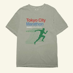 May include: A sage green t-shirt with the text "Tokyo City Marathon" in red and blue, and Japanese text. A green runner graphic is on the right. The shirt has a vintage look.