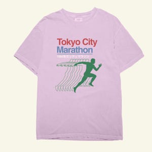 May include: A pale purple t-shirt with the words "Tokyo City Marathon" in red and blue, and Japanese text. A green silhouette of a runner is shown with motion lines, suggesting speed and movement.