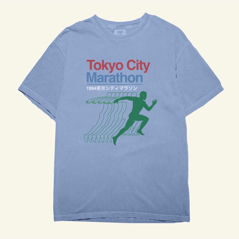May include: A pale blue t-shirt with the words "Tokyo City Marathon" in red and blue, and a green running figure graphic. The shirt also features the year "1994" and Japanese text. The design is printed on a short-sleeved tee.