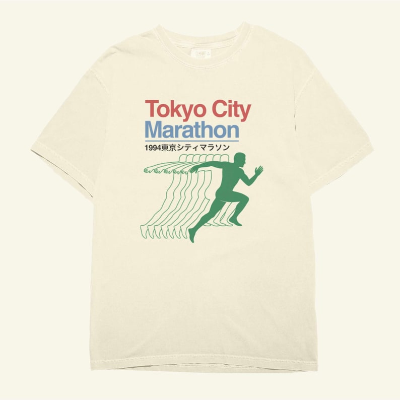 May include: A cream-coloured t-shirt with the words "Tokyo City Marathon" in red and blue, and Japanese text below. A green silhouette of a runner is shown, with green lines trailing behind. The design has a vintage aesthetic.