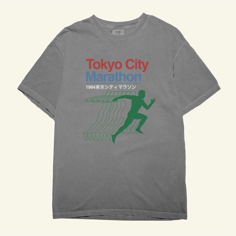 May include: Grey t-shirt featuring the text "Tokyo City Marathon" in red and blue. Below is "1994" in Japanese characters. A green runner silhouette is printed on the front, with green lines trailing behind.