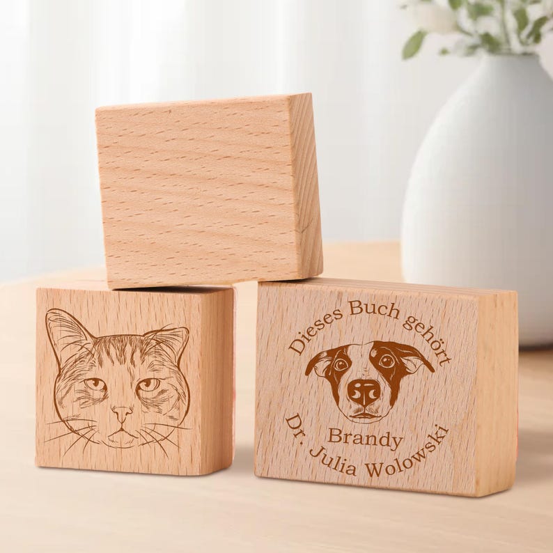 May include: Three wooden blocks with engraved images and text. The top block is blank. The middle block has a line drawing of a cat. The bottom block has a line drawing of a dog and the text "Dieses Buch geh&ouml;rt Dr. Julia Brandy Wolowksi".