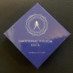 Op de afbeelding: Een donkerblauwe, ruitvormige doos met de woorden "EMOTIONAL WISDOM DECK" in het wit. De doos heeft een zilverkleurig geometrisch ontwerp met een silhouet van een persoon. De naam van de auteur staat ook op de doos.