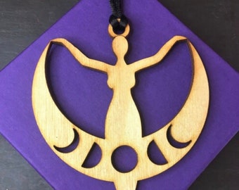 May include: Wooden ornament depicting a woman standing within a crescent moon. The moon has cutouts of various moon phases.