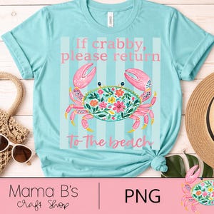 Puede incluir: Una camiseta azul claro con un dise&ntilde;o de cangrejo y el texto "If crabby, please return to the beach." El cangrejo es rosa y turquesa con detalles florales. Un sombrero de paja y gafas de sol est&aacute;n al lado.