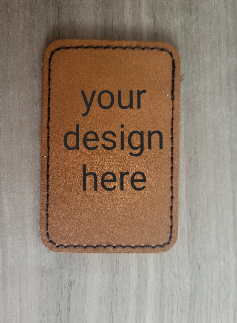 K&ouml;nnte beinhalten: Ein braunes Lederst&uuml;ck mit gen&auml;hten Kanten. Der Text "your design here" ist in Schwarz gedruckt.