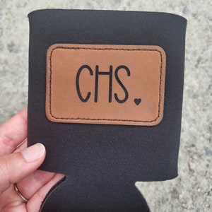 May include: Black neoprene can cooler with a brown leather patch that says "CHS."