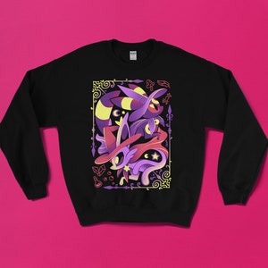May include: Black sweatshirt featuring a colorful graphic of a witchy creature with a hat, stars, and a swirling design. The artwork uses shades of purple, yellow, and pink, set within a decorative border. A cozy, long-sleeved top.