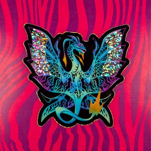 Peut inclure: Un autocollant iridescent bleu et violet représentant un dragon avec les ailes déployées. Le dragon a un design détaillé sur fond noir.
