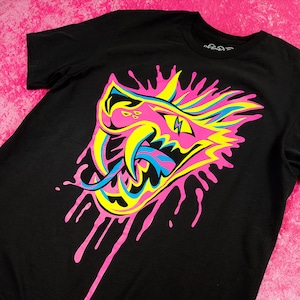 Puede incluir: Camiseta negra con un gráfico rosa, amarillo y azul de un monstruo de dibujos animados con un efecto de pintura goteando.
