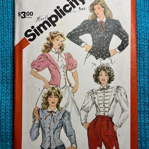 May include: Simplicity sewing pattern number 5871 for a women's blouse with a high collar and puffed sleeves. The pattern includes three different styles of blouses, each with a different fabric and color.