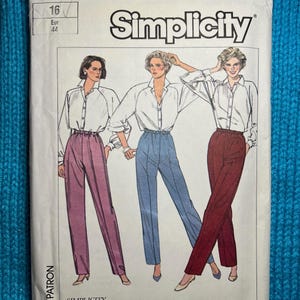 Puede incluir: Un paquete de patrones de costura Simplicity vintage con ilustraciones de mujeres con blusas blancas y pantalones de cintura alta en rosa, azul y burdeos. El paquete está etiquetado "7470" e incluye información de tallas.