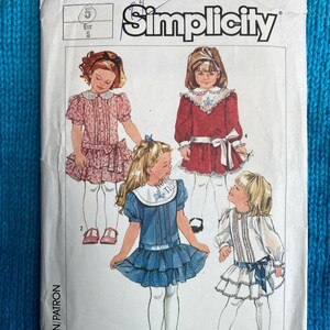 以下が含まれることがあります： 女の子用ドレスのシンシティ・ソーイングパターン番号7432。パターンには、白い襟付きのピンクの花柄ドレス、白い襟と白いサッシュ付きの赤いドレス、白い襟と白いサッシュ付きの青いドレス、白い襟と白いサッシュ付きの白いドレスの4つの異なるドレススタイルが含まれています。パターンはサイズ5〜6用です。