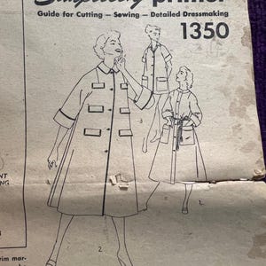 May include: Vintage Simplicity primer sewing pattern guide. The cover features illustrations of women's dresses and coats. The text reads "Simplicity primer" and "Guide for Cutting - Sewing - Detailed Dressmaking 1350". The sewing book gives complete instructions.