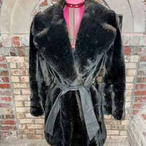 May include: A black faux fur coat with a large collar and a black leather belt.