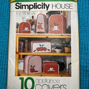 May include: Simplicity House sewing pattern for 10 appliance covers. The pattern features a red, white, and green color scheme with apple appliques. The pattern includes blue wax transfers for appliques.