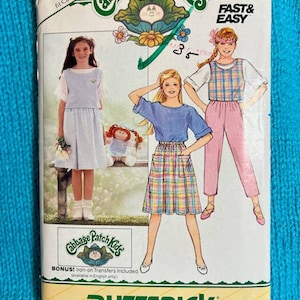 Puede incluir: Un patrón de costura vintage para ropa de Cabbage Patch Kids. El patrón incluye tres atuendos diferentes: un vestido azul con un chaleco blanco, una falda a cuadros con una blusa azul y un mono a cuadros rosa y blanco con una blusa blanca. El patrón es para las tallas 7-8-10 y está etiquetado como "Rápido y fácil".