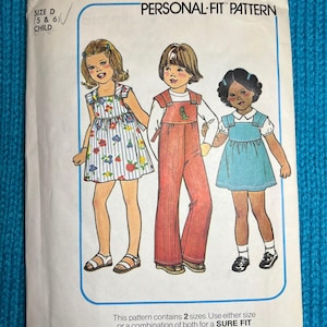 Op de afbeelding: Simplicity naaipatroon nummer 7990 voor kinderkleding. Het patroon omvat twee maten, 5 en 6, en is een "Personal-Fit" patroon. De afbeelding toont drie kinderen die de kleding stijlen dragen die in het patroon zijn opgenomen. Het patroon is verkrijgbaar in de maten B (384), C (485) en D (586).