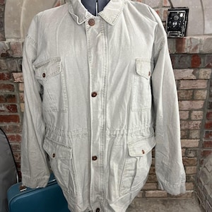 May include: A light gray utility jacket with multiple pockets and a drawstring waist.