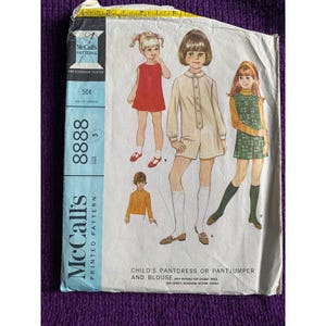 May include: A vintage sewing pattern for a child's pantdress or pantjumper and blouse. The pattern is from McCall's and is size 5. The pattern shows three girls wearing the different styles.