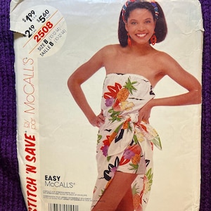 Pode incluir: Um envelope de molde de costura McCalls para um macacão sem alças com estampa tropical de abacaxis e flores. O envelope contém o texto Stitch 'N Save, 2508 e Tamanho B (10-12-14). A ilustração mostra um macacão sem alças com laço na cintura.