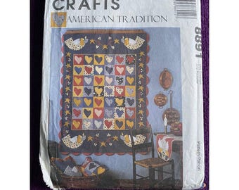 Könnte beinhalten: Ein McCall's Crafts-Muster für eine Steppdecke mit einem Herz-Design. Das Muster heißt "American Tradition" und die Musternummer ist 8891. Die Steppdecke besteht aus Stoffresten in Rot, Weiß, Blau, Gelb und Grün. Die Steppdecke hängt an einer Wand mit blauem Hintergrund. Rechts von der Steppdecke hängen zwei kleine Kupfertöpfe an der Wand.