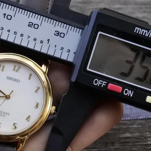 Op de afbeelding: Een gouden Seiko Lucent Paris horloge met een witte wijzerplaat en zwarte wijzers. Het horloge wordt gemeten met een digitale schuifmaat die 35,2 mm aangeeft.