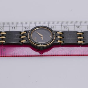 Könnte beinhalten: Eine schwarz-goldene Armbanduhr mit schwarzem Zifferblatt und goldenen Zeigern. Die Uhr hat ein schwarz-goldenes Metallband.
