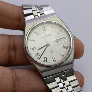 May include: A silver Seiko Lord Quartz watch with a white face and silver hands. The watch has a silver metal band and a date window that displays "WED 30".