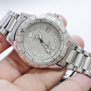 May include: A silver Casio watch with a light gray face, featuring a date window and luminous markers. The watch has a stainless steel band and a rotating bezel. The watch is water resistant to 10 bar.