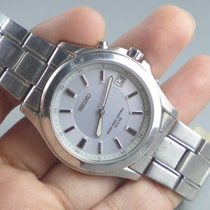 Könnte beinhalten: Eine silberne Seiko Armbanduhr mit hellgrauem Zifferblatt. Die Uhr verfügt über eine Datumsanzeige auf 3 Uhr und ein silbernes Gliederarmband. Auf dem Zifferblatt stehen die Wörter "SEIKO" und "RADIO WAVE CONTROL SOLAR".