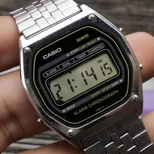 May include: A silver Casio digital watch with a black face and a silver metal band. The watch displays the time, date, and has features for alarm, dual time, timer, and chronograph.