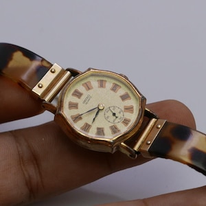 May include: A gold-toned wristwatch with a white face and Roman numeral hour markers. The watch has a brown and black tortoiseshell band and says "SEIKO QUARTZ" on the face.