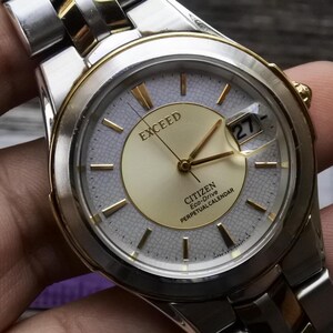 May include: A silver and gold Citizen Exceed Eco-Drive Perpetual Calendar watch with a white face and gold hands. The date window shows the number 27.